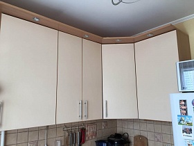 молочного цвета подвесные шкафы с подсветкой на козырьке двухцветной мебельной стенки на кухне современной квартиры молодоженов