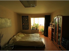 модульная картина над кроватью со светлым стеганным покрывалом и подушками в спальне, совмещенной с балконом в трехкомнатной квартире