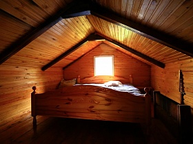небольшое окно над деревянной кроватью на ухоженной мансарде небольшого деревянного домика отшельника среди новостроек