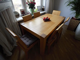 свежие фрукты в тарелке на деревянном столе, красные розы в вазе и фотографиями на белом подоконнике окна светлой гостиной современной трехкомнатной квартиры