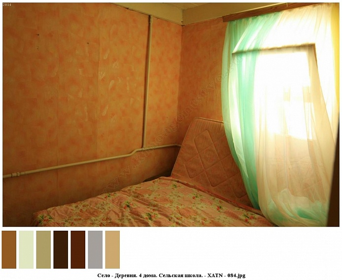 стеганное цветное покрывало на тахте у бежевых стен спальной комнаты с белой гардиной на окне жилого дома на селе