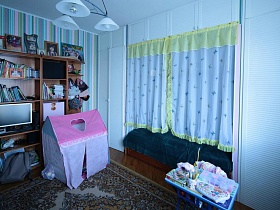 игровой домик и красочный столик на ковре, кровать в нише за шторками в детской комнате семейной трехкомнатной квартиры