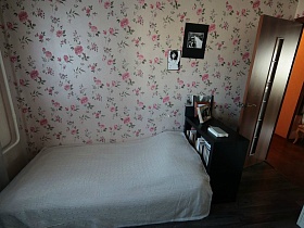 белое покрывало на большой кровати с черной тумбой и книгами на ее полках в спальне с цветочными обоями квартиры оператора