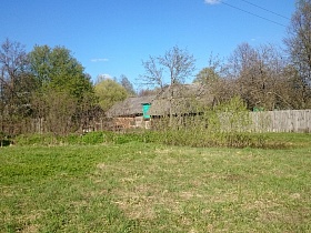 открытая поляна с зеленой травой перед жилыми домами за штакетным забором в старой деревне Троица