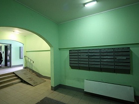 ряд темно зеленых почтовых ящиков на стене просторного освещенного холла в подъезде современной многоэтажки