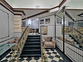 Золотая лестница с черными мраморнымиступенями в большом мраморном зале с шахматным полом