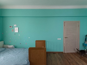 фотографии в белых рамках над кроватью с голубым покрывалом и подушками, настенная вешалка с сумочками за дверью бирюзовой спальни современной квартиры