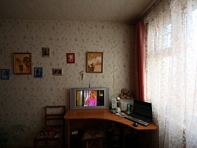 серебристый телевизор, принтер и ноутбук на поверхности углового компьютерного стола у стены с картинами и фотографиями в рамках спальной комнаты просторной современной квартиры пенсионеров