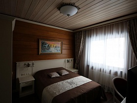 большая кровать с белоя спинкой и белыми прикраватными тумбочками в спальне съемного коттеджа