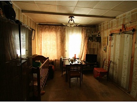 полированный стол и стулья у окна с коричневыми шторами и телевизором в углу гостиной на даче