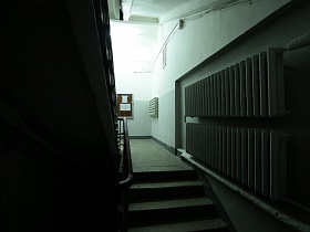 секции отопительной системы на стене серого подъезда с лестницей, ведущей на этажи дома эпохи СССР