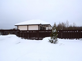 высокий коричневый деревянный забор вокруг современного съемного коттеджа зимой