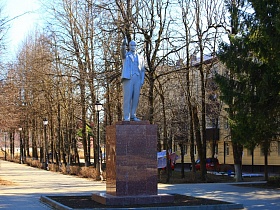 памятник Ленину на гранитном постаменте на площади рядом с многоэтажным желтым жилым домом в Сычево