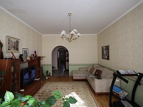 светло серый угловой мягкий диван с подушками,мебельная горка,картины на светлых стенах гостиной большой семейной квартиры на втором этаже жилого дома в Марьино