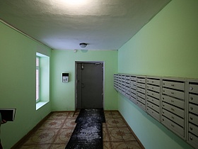 ряды серых почтовых ящиков многоэтажного дома на салатовых стенах просторного холла с дорожкой на полу с квадратной плиткой