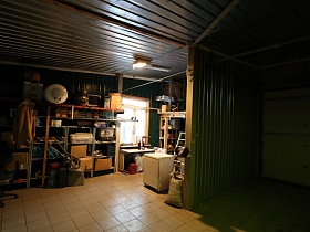 общий вид зеленого гаража с многообразными вещами на полу и полках стеллажа