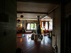 просторная гостиная с камином в центре, мебелью, многочисленными вещами и игрушками на полу деревянного загородного дома