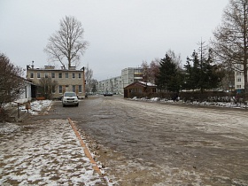 широкая автомобильная дорога в жилом квартале вдоль сквера и торговых точек за площадью у ДК СССР в зимнее время