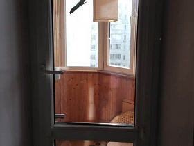 подвесная люстра, плетенное кресло на полу с ковриком застекленного балкона трехкомнатной квартиры с дизайнерским ремонтом