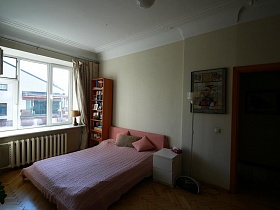 соседний дом из окна с бежевыми шторами светлой спальни с большой розовой кроватью стильной квартиры художественного образца
