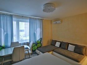 угловой диван в бежево серых тонах с подушками у окна с дизайнерскими голубыми шторами в молодежной евро квартире