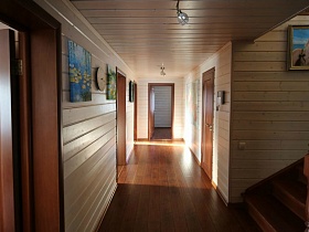 картины и часы на стенах светлого холла с дверьми в различные комнаты современого деревянного дома