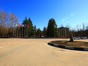 флагшток по обе стороны центральной площади за кольцевым перекрестком с символом мудрости на круглой клумбе в городке Сычево