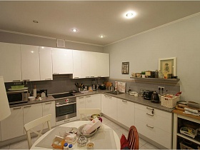 разнообразные кухонные предметы на серой столешнице белой кухни в просторной современной трехкомнатной квартире