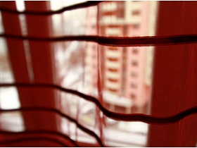 красная прозрачная гардина с коричневой полоской на окне восточной спальни простой двухкомнатной квартиры на третьем этаже