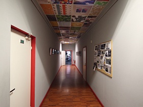 яркий разноцветный потолок, стенд с фотографиями и многочисленные рамки под стеклом на серых стенах офисного коридора с открытой дверью в кафе