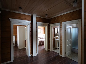 просторный деревянный холл с открытыми дверьми в разные комнаты современного съемного коттеджа