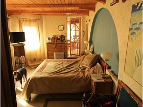 диван, прикроватные тумбочки, большая кровать у светлой стены с бра и картиной в спальной комнаты необычного дома для съемок кино