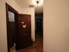 люстра в стиле хай-тек на потолке просторной прихожей с наклеенными картинками на коричневой межкомнатной двери современной белой евро квартиры в красном доме