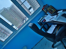 компьтерное кресло у столика с книгами и ноутбуком на застекленном балконе молодежной евро квартиры Новостроя