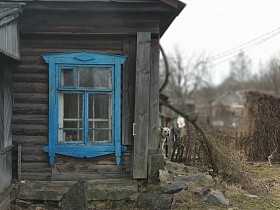 окно с решеткой и голубым деревянным наличником на бревенчатой стене многоквартирного барачного дома Акуловки на тофоразработках