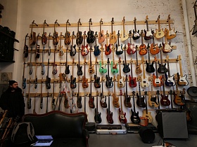 ряды электро и электро акустических гитар на ровных рядах деревянных креплений у белой стены стильного музыкального магазина с большим окном
