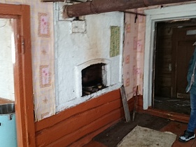 русская побеленная печь в углу комнаты с окрашенными дверными лутками и деревянным полом дома в заброшенной деревне