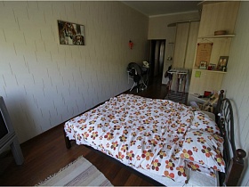 простой коврик у кровати с постельным в цветочек и серый телевизор в углу спальни квартиры педагога