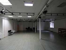 общий вид белого танцевального зала с софитами и лампами дневного освещения на белом потолке, черными стульями вдоль стены в подземелье со сводами для съемок кино