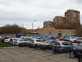 многочисленные машины на стоянке у открытой площадки с квадратной плиткой перед двухэтажным зданием столовой