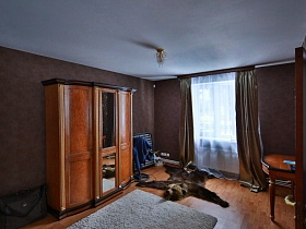 коричневый шкаф для одежды с зеркалом посередине, раскладушка у коричневой стены спальни добротного кирпичного дома