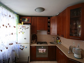 белый холодильник у окна с белой гардиной и коричневая кухня в квартире областного квартала