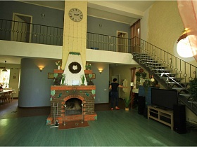 просторная гостиная с камином посередине, лестницей у стены, ведущей на второй этаж и балконом с перилами в современном доме для съемок кино