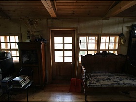 деревянный диван,шкаф,книги на стуле, лопата у входной двери деревянного домика на дачном участке