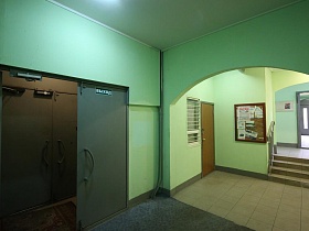 плитка и ковровое покрытие на полу у железных дверей зеленого подъезда на выходе из холла жилого дома