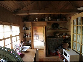 микроволновка на стуле, деревянный стол у окна, полки с посудой у входной двери в деревянный домик на дачном участке