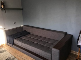 серый мягкий раздвижной диван у серой стены юношеской комнаты трехкомнатной квартиры с дизайнерским ремонтом