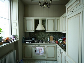 белый шкаф и белая кухня с зеленой мозаичной плиткой рабочей поверхности и столешницы с разными кухонными предметами в зоне кухни с окном в девчачьей дизайнерской квартире