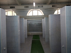ряд простых открытых душевых кабин по обе стороны зеленой дорожки ведущей к лестнице с бассейном в просторной комнате лофт здания для съемок кино