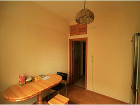 овальный деревянный стол на ножке, стулья и зеленый с желтым абажур люстры в кухне типичной двухкомнатной квартиры